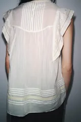 Blusa blanca sin mangas confeccionada en hilatura con viscosa y algodón. Tiene cuello redondo, detalle de bordados a contraste y cierre en espalda con abertura y botón.