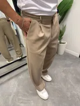 Pantalón sastrero de corte baggy, color beige, con pinzas frontales, bolsillos laterales y cierre frontal con botón.