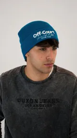 Gorro tipo beanie de tejido acanalado en color azul, con bordado frontal en color blanco que incluye la frase 'off-court' y detalles de marca.