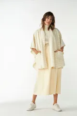 Ruana corta de lana virgen color beige con diseño a cuadros finos oscuros y bolsillos frontales aplicados.