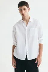 Camisa H&M de corte relajado, confeccionada en tejido liviano de mezcla de lino y algodón color blanco. Presenta cuello inglés, cierre frontal de botones, manga larga con puños ajustables y bolsillo aplicado en el pecho.