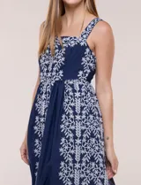 Vestido midi azul marino con bordados florales blancos, escote cuadrado, breteles anchos y falda amplia con bolsillos.