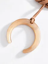 Collar largo con tira de cuero sintético marrón y dije en forma de herradura de resina marmolada en tono beige.
