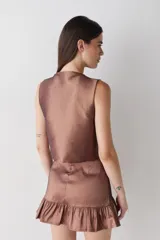 Top sin mangas de estilo cruzado, confeccionado en tela satinada color cobre. Presenta un diseño corto con cierre frontal mediante tiras finas para anudar y cuello redondo.