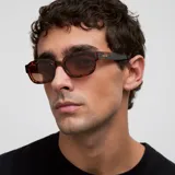 Lentes de sol con montura gruesa de acetato color carey (tortoise) y forma ligeramente cuadrada/ovalada. Los lentes son polarizados de color marrón.