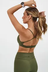 Top deportivo color beige con contorno inferior y tiras cruzadas en la espalda color borgoña. Cuenta con almohadillas removibles.