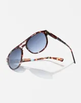 Lentes de sol Hawkers modelo Diver, con armazón de acetato en estampado carey con detalles en azul y cristales degradados en tono azulado. Diseño estilo aviador con doble puente.