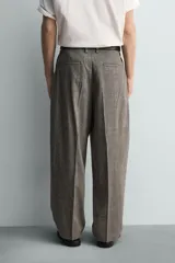 Pantalón de corte relajado con diseño de cuadros, confeccionado en tejido con lana. Presenta cintura con pliegues frontales, bolsillos laterales y bolsillos traseros de vivo, con cierre frontal de cremallera y gancho metálico oculto.