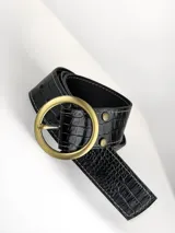 Cinto de cuero negro con textura de reptil, hebilla circular metálica en tono bronce envejecido y detalles de remaches metálicos.