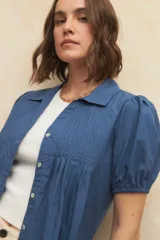 Camisa roja con cuello clásico, mangas cortas abullonadas y cierre frontal con botones.