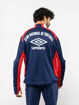 Buzo de entrenamiento Umbro del Club Nacional de Football, con cierre frontal parcial y cuello alto. Presenta un diseño con bloques de color azul, blanco y rojo, con panel frontal acolchado y mangas largas con aberturas para pulgares.