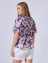 Blusa de gasa estampada con flores rosas y verdes sobre fondo azul marino. Escote bote con punto smock y mangas cortas amplias.