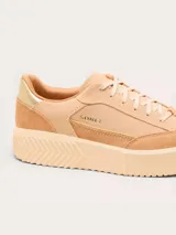 Championes Sorel modelo Ona Ave T-Toe, color beige con detalles en gamuza y cuero. Presenta suela de plataforma con diseño estriado y detalle metálico dorado en el talón.