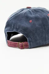 Gorra tipo baseball con diseño bicolor, cuerpo en azul desgastado y visera en color bordó. Presenta ojales de ventilación bordados en contraste y botón superior a tono con la visera.