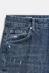 Jeans baggy de tiro medio con cinco bolsillos, trabillas para cinto y cierre frontal con cremallera y botón metálico. Cuenta con detalle de aplicación de brillos en toda la prenda.