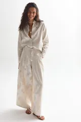 Pantalón culotte color marfil con estampado floral en brocato, de tiro alto con tablas, piernas anchas, bolsillos laterales y cierre frontal escondido.