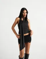 Top halter asimétrico negro con drapeado que incluye una caída larga de tela sujeta por una hebilla metálica en el hombro, frunces laterales y espalda descubierta.