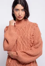 Sweater tramado color salmón, de cuello alto y manga larga abullonada con puños. Presenta detalle de flecos en el frente.