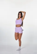 Conjunto deportivo de dos piezas color lila, compuesto por un top deportivo con escote redondo y espalda estilo nadador, y un short de tiro alto ajustado. Ambas prendas presentan el logo de la marca estampado en blanco.