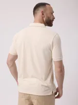 Remera tipo polo color beige, de manga corta y corte clásico, con cierre parcial frontal con cremallera.