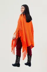Poncho rojo de tejido artesanal con aplique central de crochet en forma de mandala con tonos amarillos, blancos y rojos. Presenta terminación con flecos en los laterales y diseño holgado.
