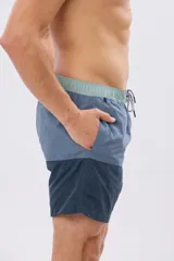 Short de baño con diseño de bloques de color en tonos celeste y azul marino, con cintura elástica en color verde claro y cordón ajustable.