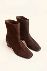 Bota de caña media confeccionada en cuero vacuno negro, con diseño minimalista y cierre trasero. Presenta un taco cilíndrico de madera tallada y punta cuadrada.