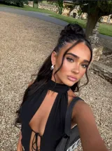 Top negro de estilo halter con cuello alto y abertura frontal profunda, ajustado mediante lazos. Confeccionado en tela semitransparente y ligera.