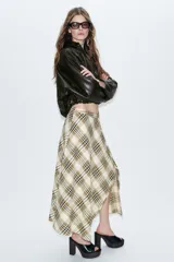 Falda midi de tiro alto con estampado de cuadros en tonos beige, marrón y negro. Presenta un diseño asimétrico con abertura frontal y detalles desflecados en el bajo.