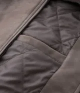 Campera de material sintético en color gris topo, con cuello inglés, cierre frontal por cremallera, mangas largas con puños elásticos y diseño de relieve tribal en la espalda.