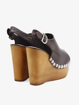 Sandalias de cuero negro con cuña alta de madera y plataforma delantera, detalle de tachas metálicas en los laterales y tira con hebilla en el talón.