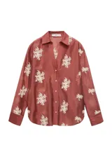 Camisa de manga larga en color terracota con diseño semitransparente. Presenta cuello camisero, cierre frontal con botones y bordados florales en color blanco distribuidos por toda la prenda.