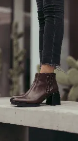 Bota corta de cuero color marrón, con diseño de silueta limpia y sofisticada. Presenta detalles texturados en el lateral y un taco ancho de bloque color negro que brinda estabilidad.