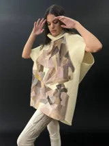 Poncho de lana merino afieltrada con cuello alto y mangas cortas. Diseño tipo mosaico con piezas geométricas en tonos verde azulado y gris.