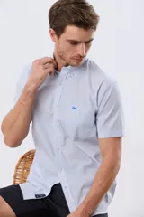 Camisa de manga corta a rayas celestes y blancas, con cuello abotonado, bolsillo frontal en el pecho con logo bordado y cierre frontal de botones.