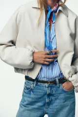 Chaqueta bomber negra con cuello solapa, manga larga abullonada y puños elásticos. Presenta falsos bolsillos de doble vivo en la parte delantera y cierre frontal con cremallera.