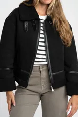 Campera tipo gamulán color negro, con interior y detalles en cuello y puños de corderito sintético. Presenta cierre frontal, detalles en cuero sintético y corte oversize.