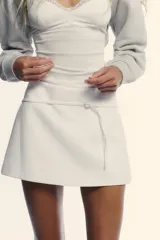 Falda pantalón de tiro medio en color blanco, con diseño minimalista y detalle de cinturón fino integrado con hebilla metálica. Cuenta con cierre lateral mediante cremallera oculta.