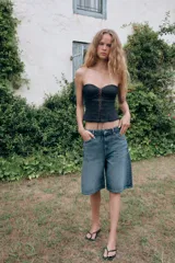 Bermuda baggy de denim azul con tiro medio, trabillas para cinturón y diseño de cinco bolsillos. Presenta cierre frontal con cremallera y botón metálico.