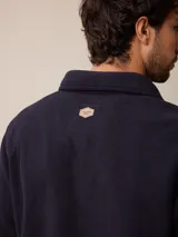 Sobrecamisa de polar azul marino con cierre frontal de botones a presión. Presenta bolsillos frontales con solapa, uno de ellos con cierre de cremallera adicional y detalles en contraste de material técnico.