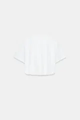 Camiseta cropped blanca de algodón 100%, con cuello redondo, manga corta y bajo abullonado con pliegues.