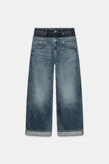 Jeans de tiro bajo confeccionados en denim, con diseño holgado y bajo con vuelta. Presentan el detalle de doble cinturilla en tonos contrastantes de azul, cierre frontal con cremallera y botón metálico, y cinco bolsillos clásicos.