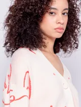 Cardigan corto de tejido de punto color crema con diseño de caras abstractas en azul, escote en V, manga larga y tres botones de plástico.