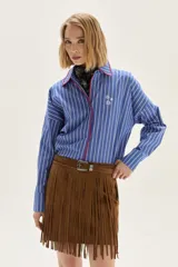 Camisa de corte holgado con diseño de rayas verticales en azul y blanco. Presenta cuello clásico y cartera frontal con detalles bordados en hilo rojo. Incluye un pequeño bordado de estrellas en el pecho y mangas largas con puños estructurados.