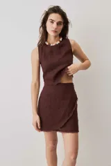 Falda cruzada tipo wrap color beige, de lino, con diseño asimétrico y bordes deshilachados. Cuenta con cierre de botón en la cintura.