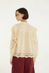 Blusa de mangas largas con puños abotonados, cuello alto con detalles de encaje y cierre frontal de botones forrados, confeccionada en tejido liviano con aplicaciones caladas.
