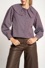 Camisa a cuadros azul y rosa con cuello babero, mangas largas abullonadas y cierre frontal con botones.