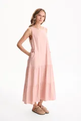 Vestido largo fluido de lino color rosado, sin mangas, con escote redondo y falda amplia con volados en niveles y bolsillos laterales.