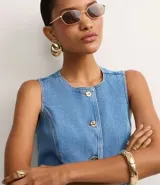 Chaleco de jeans azul oscuro, sin mangas, con cuello redondo y cierre frontal de botones blancos. Presenta un corte ligeramente alargado y solapas frontales que simulan bolsillos.