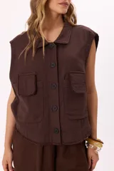 Chaleco marrón estilo cargo con lavado suave, cuello camisero, cierre frontal con botones negros, bolsillos frontales y ruedo desflecado.